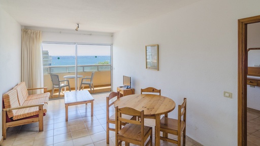 Salón de los Apartamentos Durazno Sur con mobiliario funcional: mesa, sillas, sofá y TV, acceso al balcón y vistas al mar